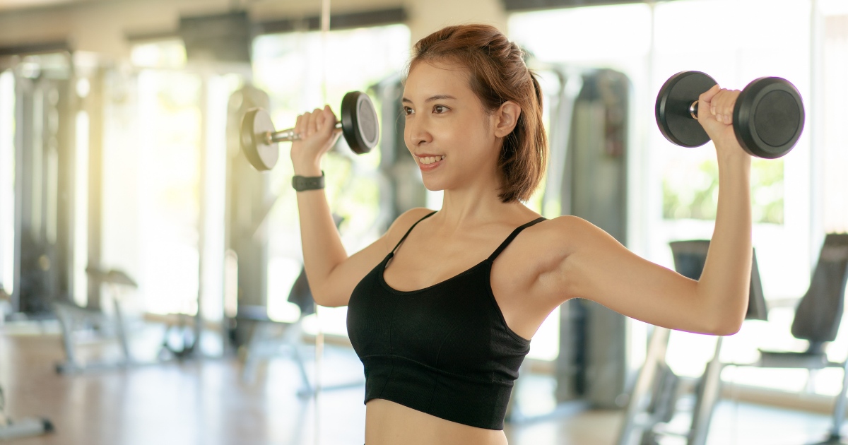 woman gently lifting light weights in a bright gym, smiling