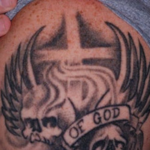 Black ink tattoo of wings, skull, "of god", and cross before laser tattoo removal.